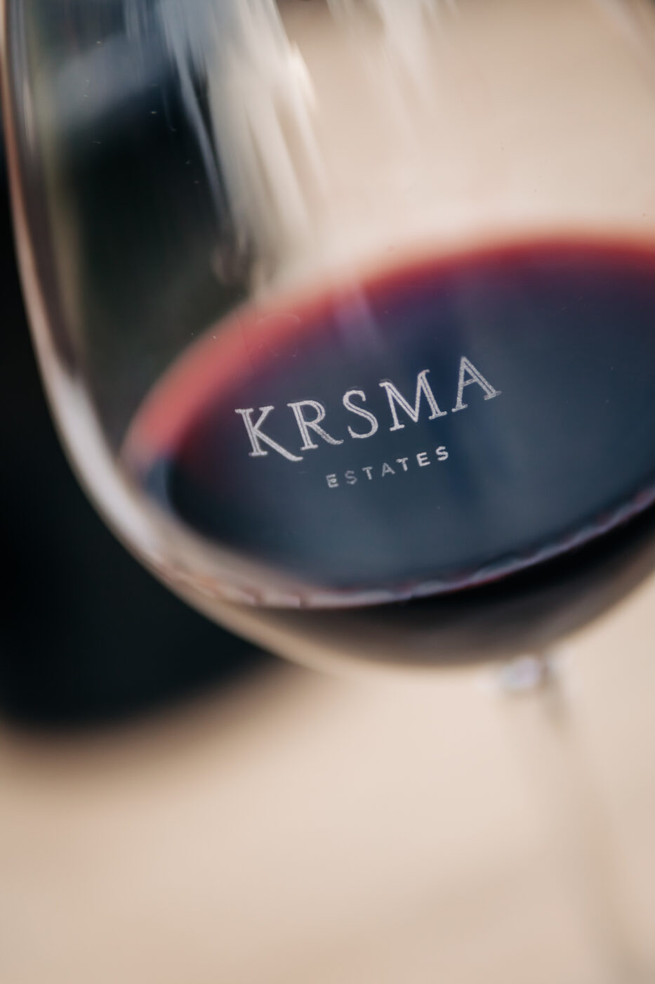 A close-up photograph of a wine glass filled with red wine, with emphasis on the logo of KRSMA estates. This brand-focused image highlights refinement, identity, and the human connection at the heart of storytelling photography.